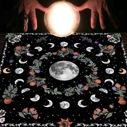 Hands holding a crystal ball over a black cloth with moon phases and floral designs.