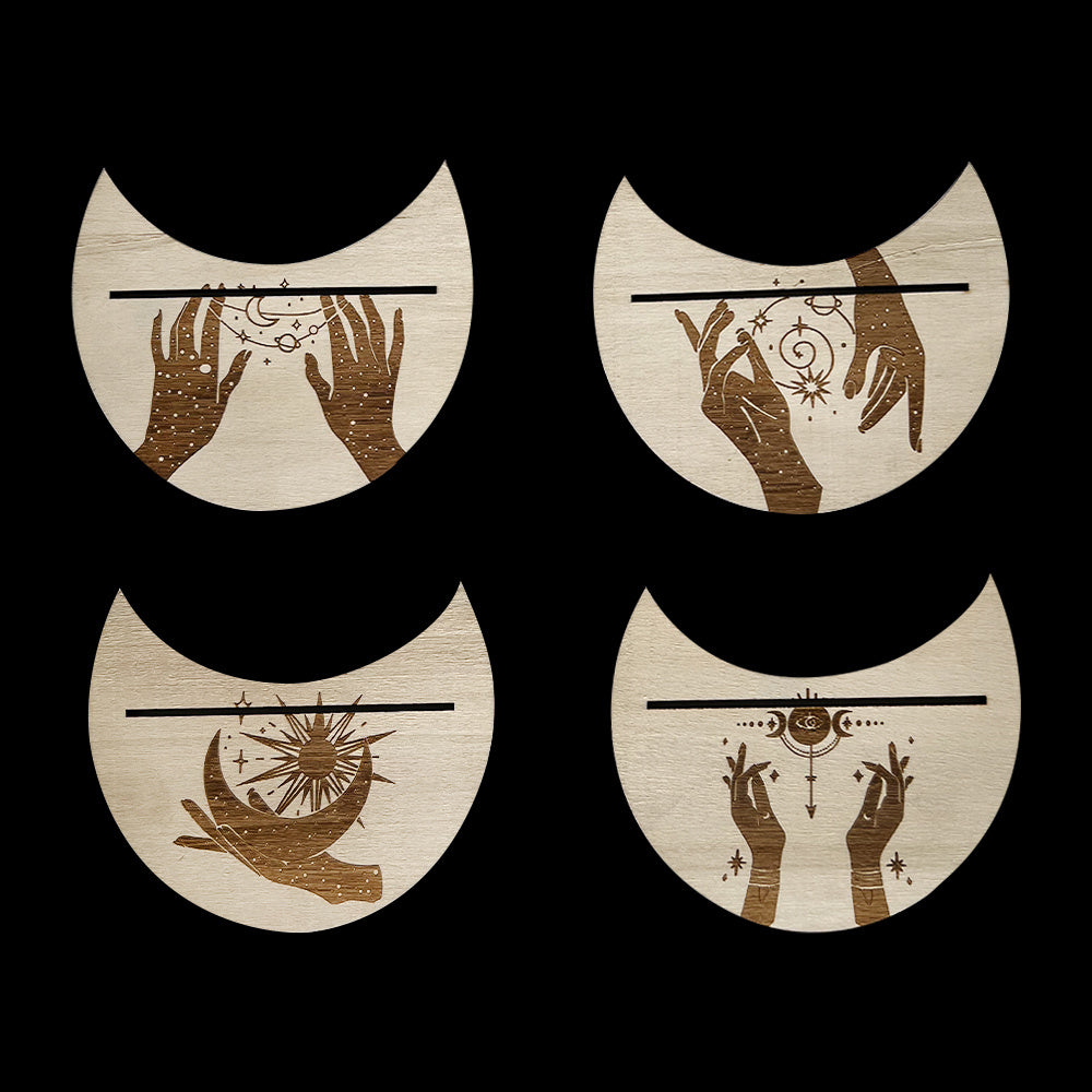 Four wooden coasters with hand designs and celestial elements on a black background