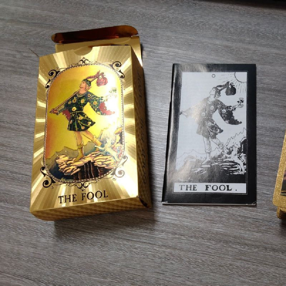 Gold and black tarot card featuring 'The Fool' on a wooden surface.