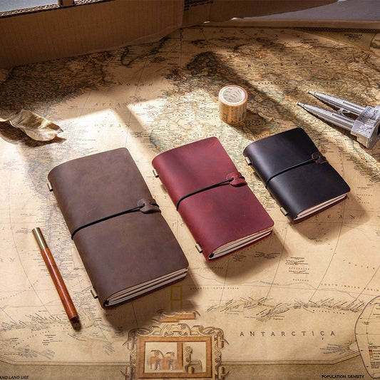 Three leather-bound notebooks in brown, red, and black on a world map with writing instruments.